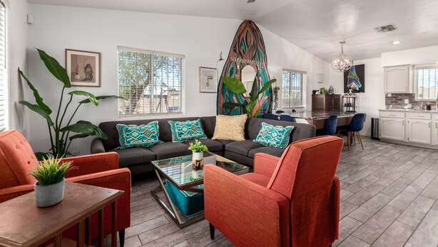 A modern living room with a sofa, chairs, a coffee table, and a dining area with a kitchen in the background.