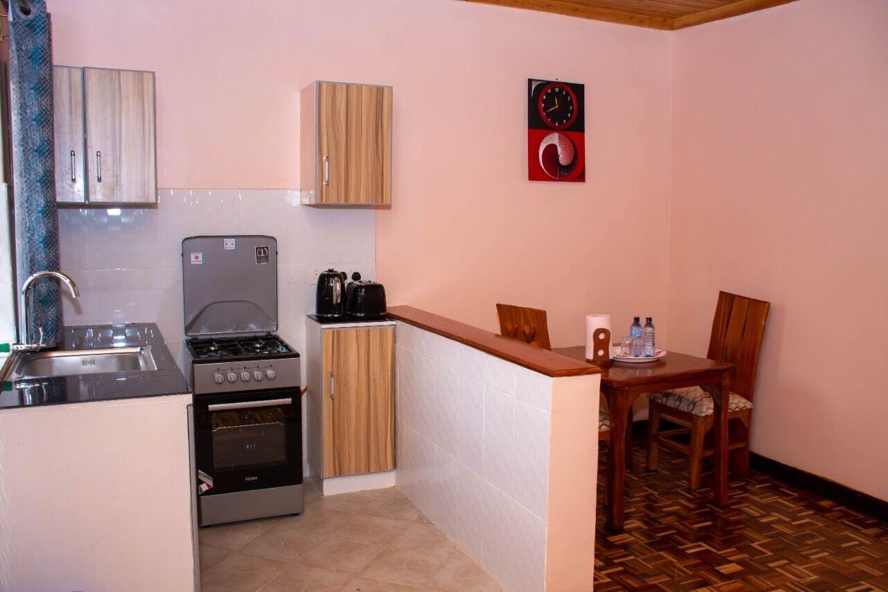 Une cuisine compacte équipée d’une cuisinière, d’un four et d’un évier, de placards en bois, d’une petite table à manger avec des chaises et d’une horloge murale.