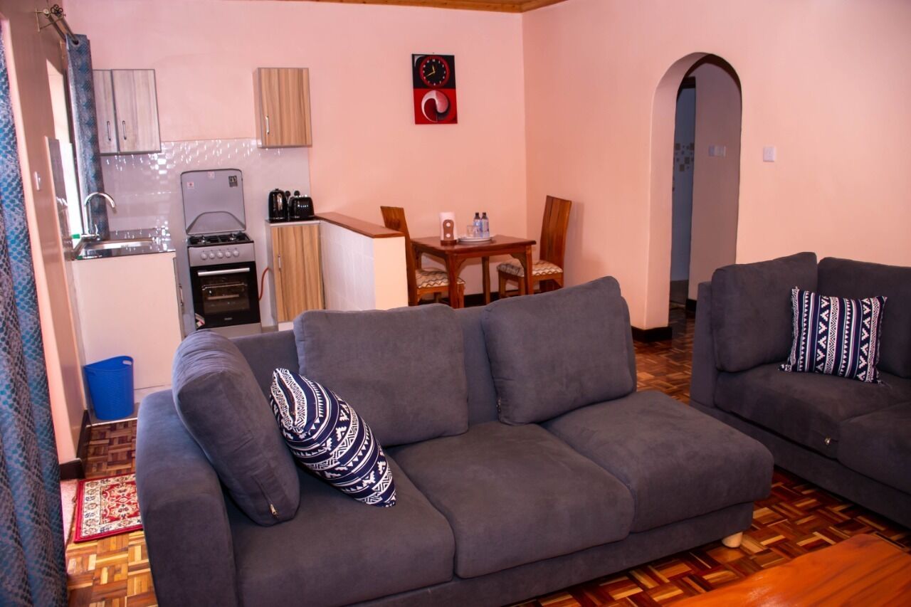 Een woonkamer met een grijze bank, een eettafel met stoelen, een keuken met fornuis en oven, en een houten vloer.