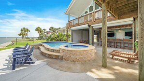 A pool area with lounge chairs and a hot tub, surrounded by a wooden deck and a large house with a balcony. - Margaritaville on the Bay by Ryson Vacation Rentals (Galveston)
