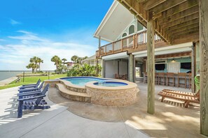 A pool area with lounge chairs and a hot tub, surrounded by a wooden deck and a large house with a balcony. - Margaritaville on the Bay by Ryson Vacation Rentals (Galveston)