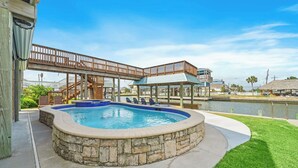 A swimming pool with stone edging, a wooden deck, and a covered area with chairs. - Margaritaville on the Bay by Ryson Vacation Rentals (Galveston)