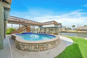 A swimming pool with stone edging, a wooden deck, and a covered area with chairs. - Margaritaville on the Bay by Ryson Vacation Rentals (Galveston)