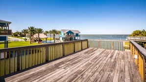 A wooden deck with a view of the ocean and a building with a blue roof. - Margaritaville on the Bay by Ryson Vacation Rentals (Galveston)