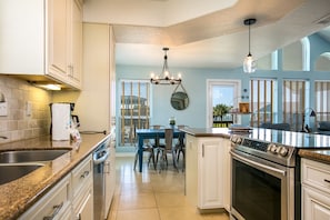 A modern kitchen with granite countertops, stainless steel appliances, and a dining area with a blue table and chairs.