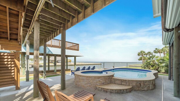 A covered outdoor area with a hot tub, wooden chairs, and a view of the ocean. - Margaritaville on the Bay by Ryson Vacation Rentals (Galveston)