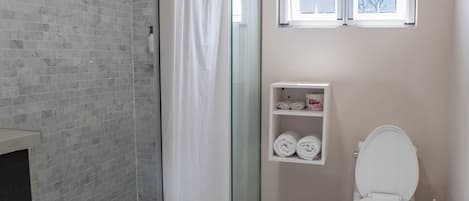 A bathroom with a glass shower enclosure, a toilet, and a shelf with towels.