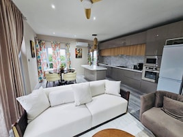 Uma sala moderna com um sofá branco, uma mesa de jantar com cadeiras e uma cozinha com fogão, micro-ondas e frigorífico.