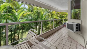 A balcony with a tiled floor, white metal railing, and a white chair. - Maui Banyan A-202 by Maui Rental Group (Kihei)