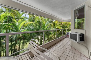 Een balkon met betegelde vloer, een witte metalen balustrade en een witte stoel.