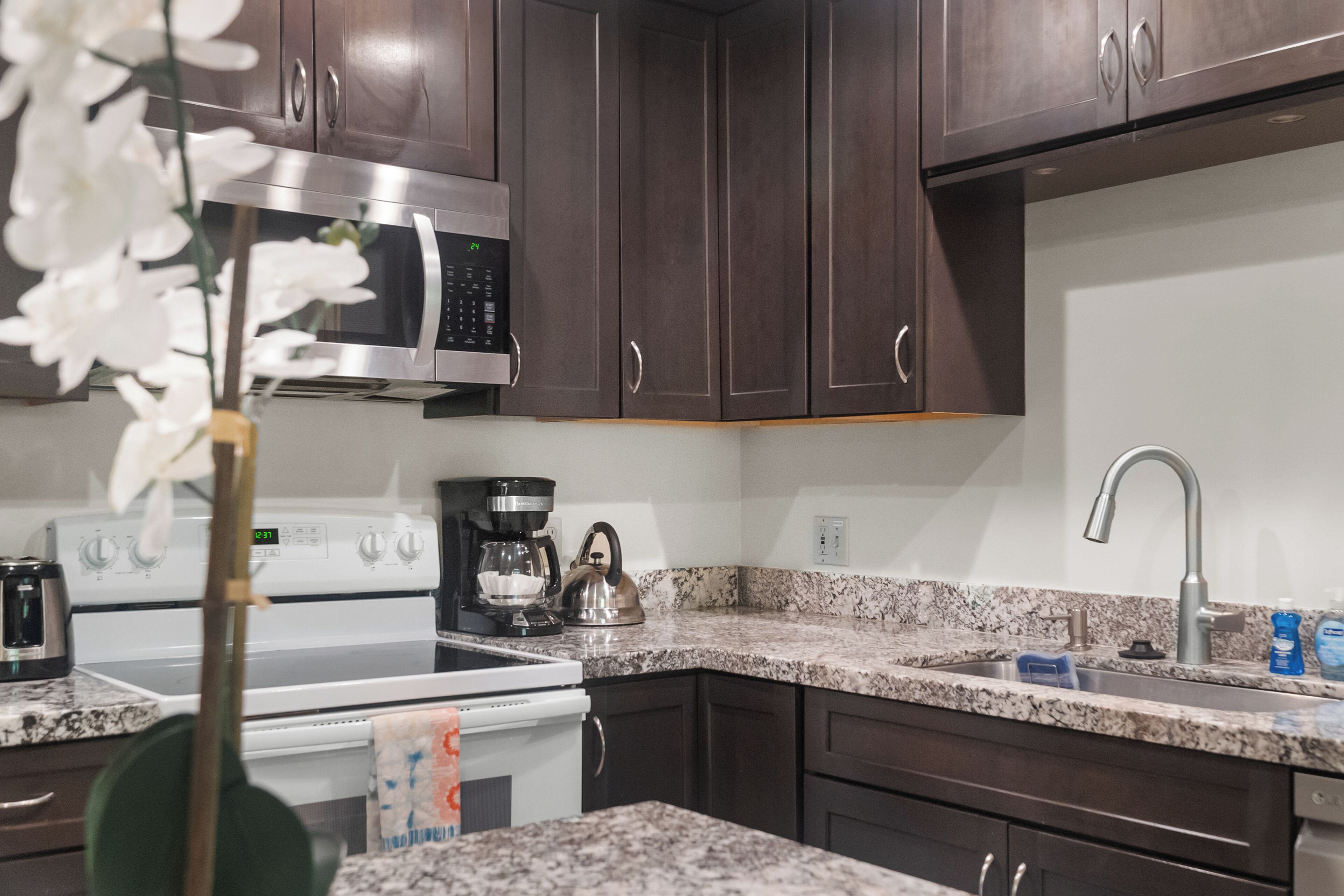 A modern kitchen with dark wooden cabinets, a stainless steel microwave, a coffee maker, and a granite countertop.