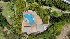 Vista aérea de una propiedad con piscina, rodeada de exuberante vegetación y palmeras.