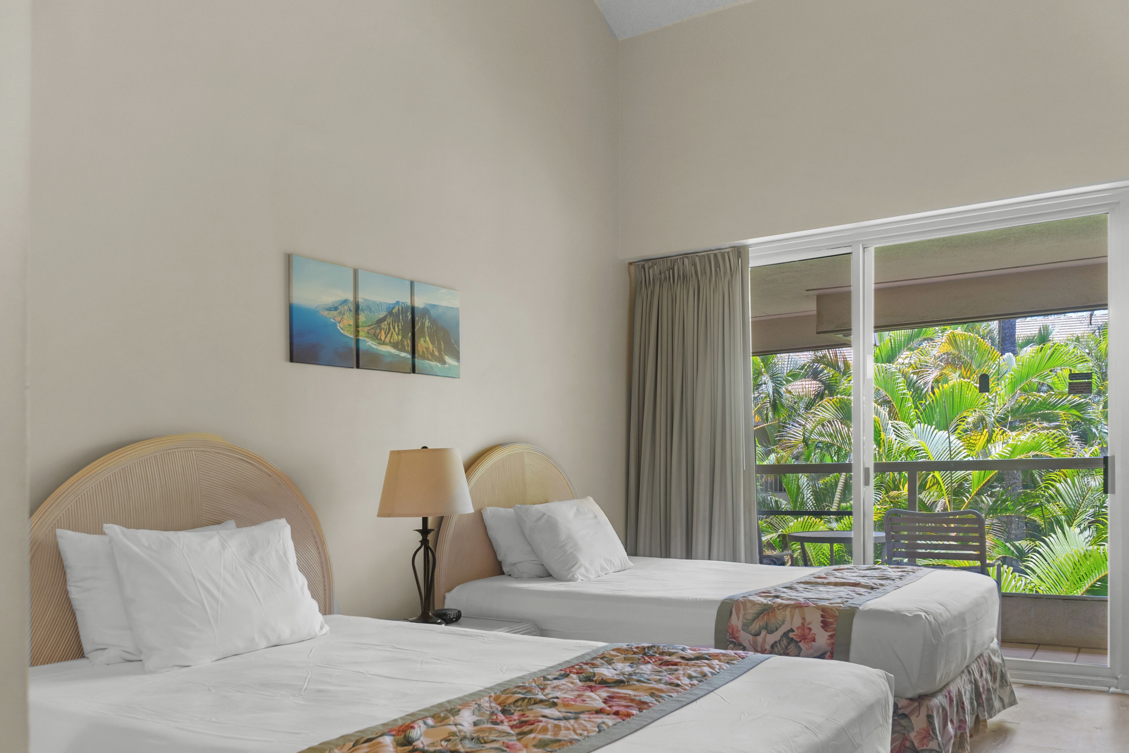 Une chambre d’hôtel avec deux lits, une grande fenêtre donnant sur une végétation tropicale et un tableau accroché au mur.