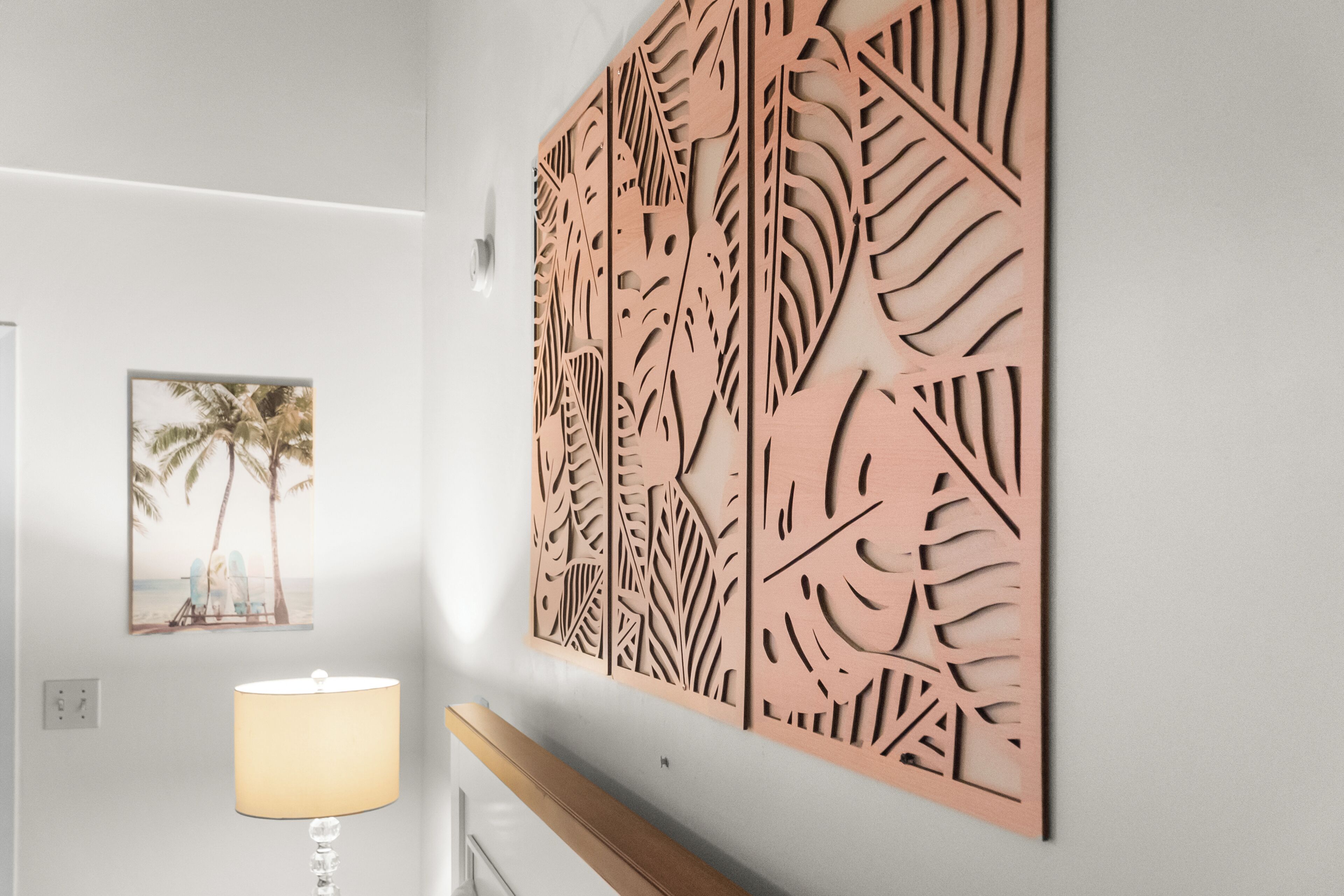 A hallway with a wooden decorative panel, a framed picture of a beach scene, and a lamp.