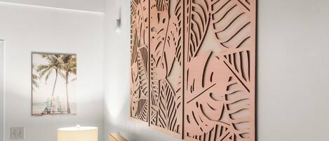 A hallway with a wooden decorative panel, a framed picture of a beach scene, and a lamp.