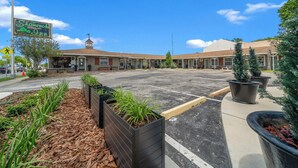 A motel with a signboard, parking lot, and landscaped areas with plants.