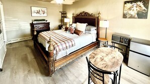A hotel room with a large bed, bedside lamps, a small table, a chair, a refrigerator, and a ceiling fan.