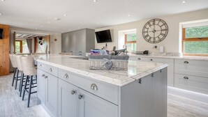 A modern kitchen with a large island, bar stools, a flat-screen TV, and a clock on the wall. - The Oak, Country Home, Sleeps 4 with Hot Tub (Oakenshaw)