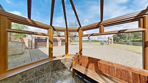 Quarto nos fundos com um banco de madeira, janelas amplas e vista para um espaço pavimentado com uma estátua.
