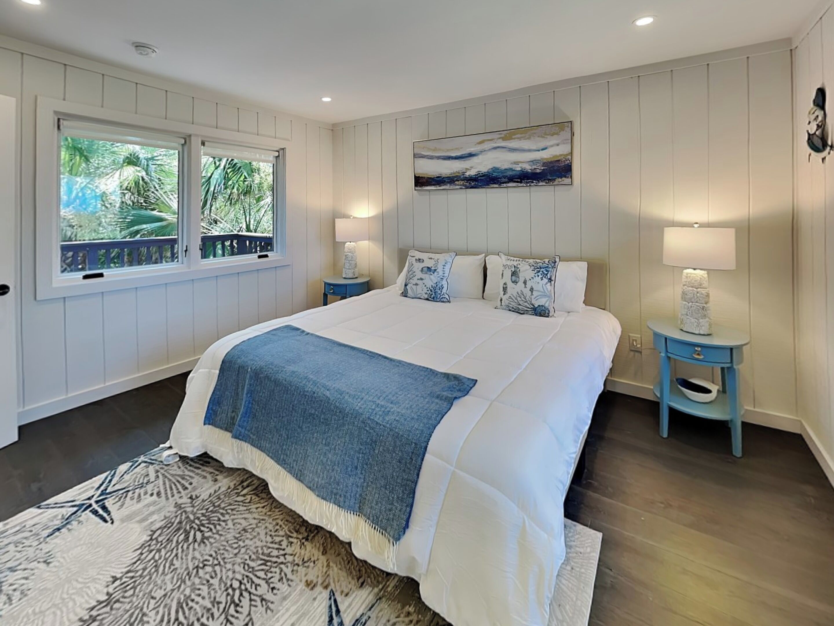 A bedroom with a large bed, two bedside tables, a window with a view, and a painting on the wall.