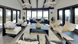 A spacious living room with a high ceiling, large windows, and a view of the ocean. - Ocean Commotion by Distinctive Beach Rentals (Ponte Vedra Beach)