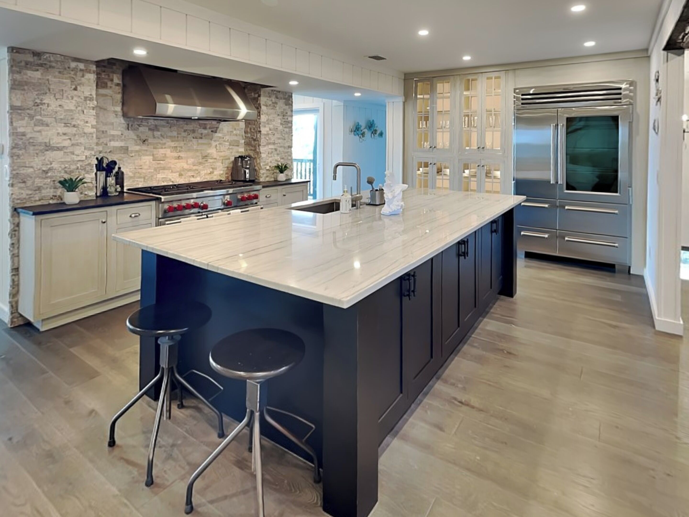 A modern kitchen with a large island, stainless steel appliances, and a stone backsplash.