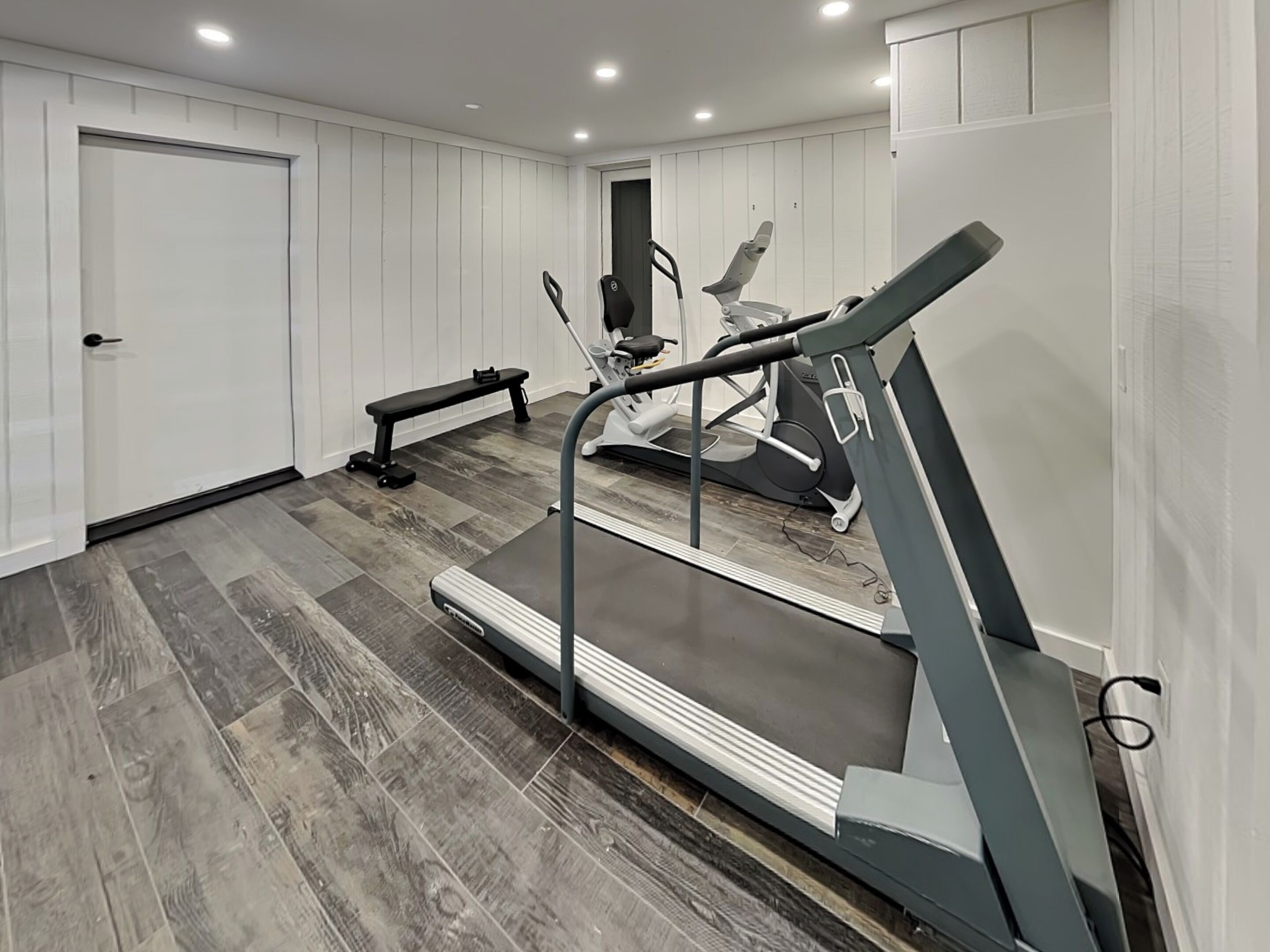 Un gimnasio en casa con cinta de correr, elíptica y banco.