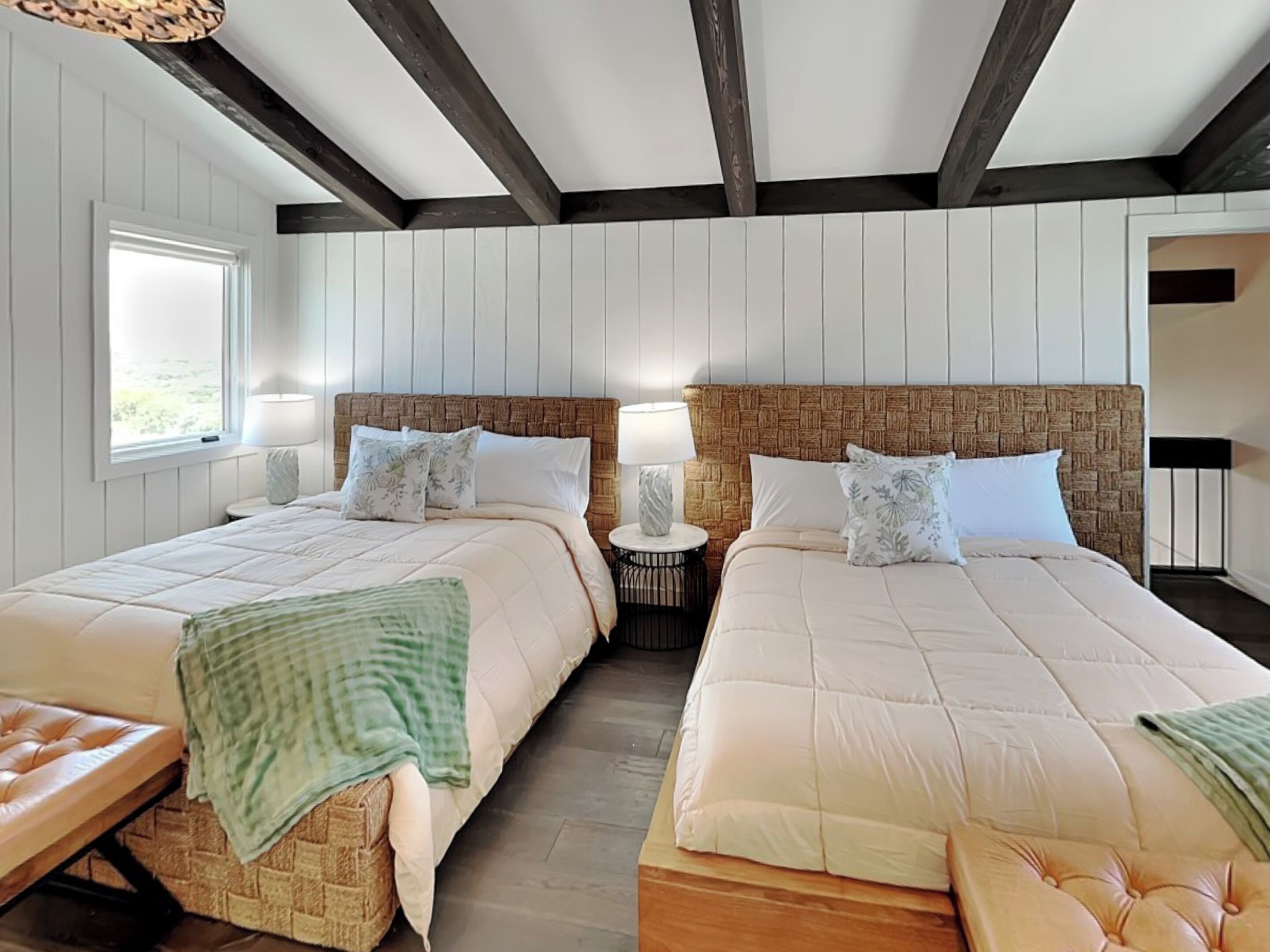 Une chambre double avec deux lits, des poutres apparentes au plafond et une fenêtre laissant entrer la lumière naturelle.