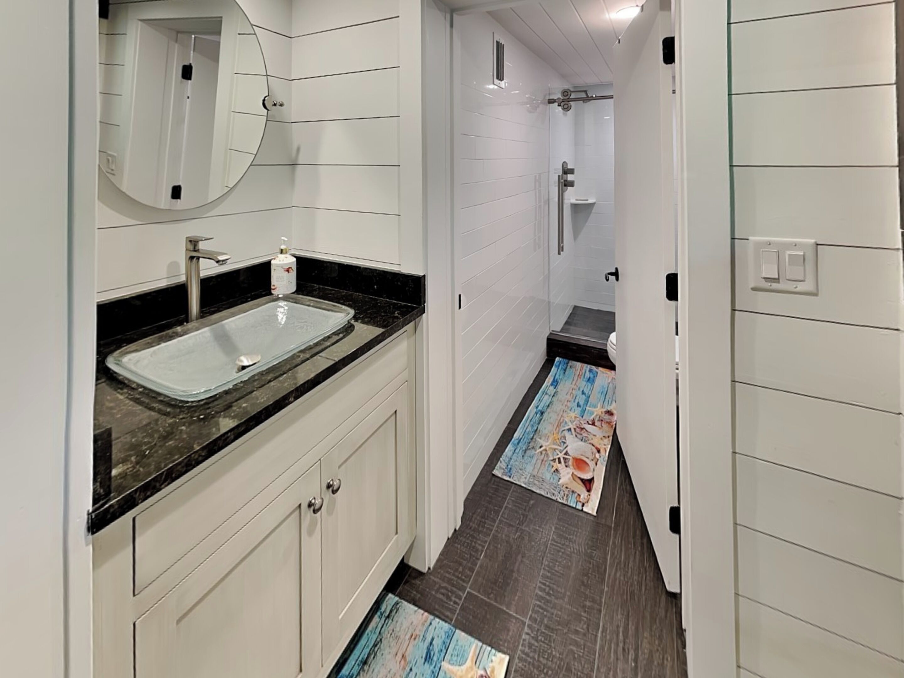 A modern bathroom with a glass sink, white cabinets, a mirror, and a shower area.