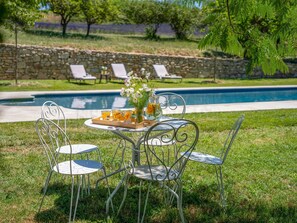 Ein Tisch mit Stühlen am Pool, eine Ablage mit Getränken und Blumen, und eine Steinsäule im Hintergrund.