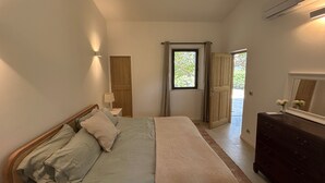 Een slaapkamer met een bed, een dressoir, een nachtkastje, een raam en een deur.