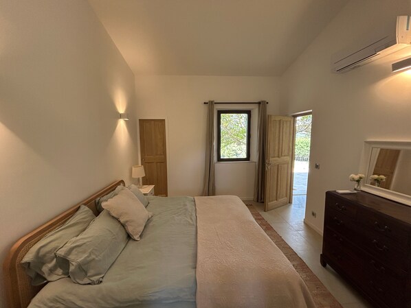 A bedroom with a bed, a dresser, a nightstand, a window, and a door.