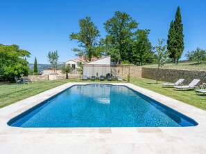 Ein rechteckiger Swimmingpool mit klarem, blauem Wasser, umgeben von einer Steinmauer, einem Rasen und einigen Bäumen.