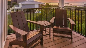 A wooden deck with two chairs and a table, overlooking a sunset with buildings in the background. - New! 5BD+Private Pool! 3 Decks with amazing views! (Gulf Shores)