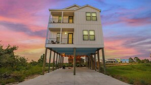 A two-story building with a balcony on the second floor, a covered walkway leading to the entrance, and a view of the surrounding landscape. - New! 5BD+Private Pool! 3 Decks with amazing views! (Gulf Shores)