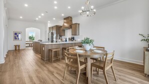 A spacious kitchen with wooden cabinets, a central island, and a dining area with wooden chairs and a table. - New! 5BD+Private Pool! 3 Decks with amazing views! (Gulf Shores)