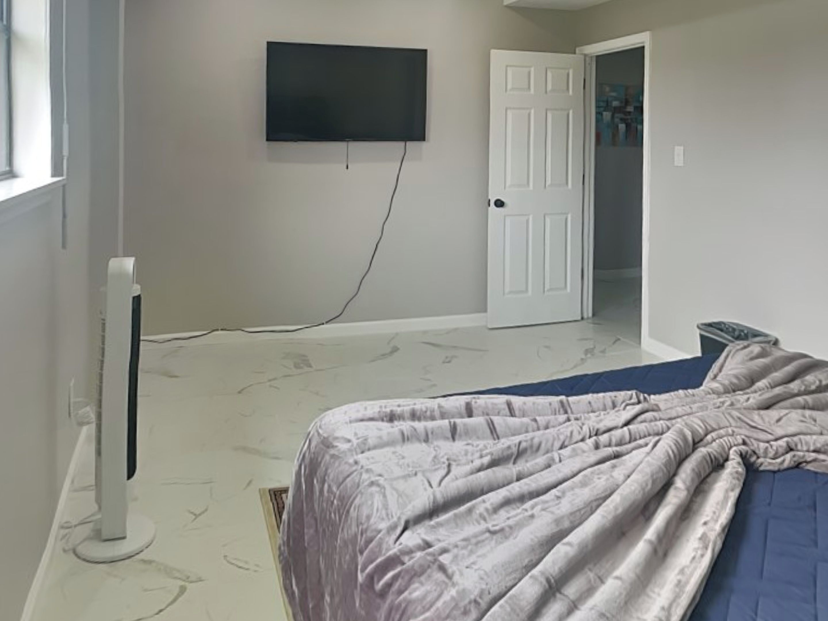 Ein Schlafzimmer mit einem Bett, einem an der Wand montierten Fernseher und einer Tür zu einem weiteren Raum.