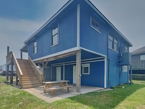 A two-story blue house with a covered patio and a wooden picnic table. - Ocean Oasis by Ryson Vacation Rentals (Galveston)