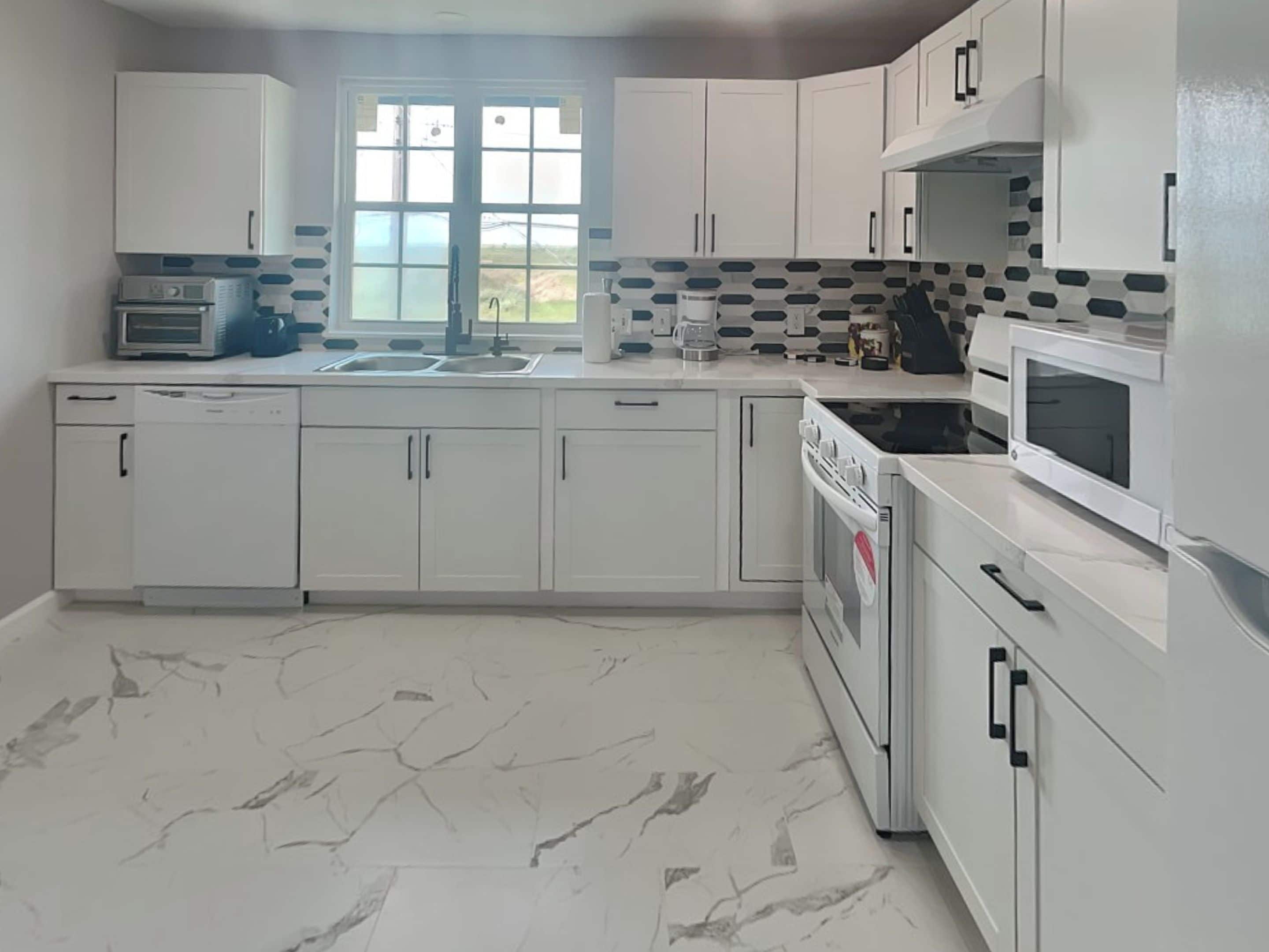 Een moderne keuken met witte kasten, een inbouwoven, magnetron en vaatwasser.