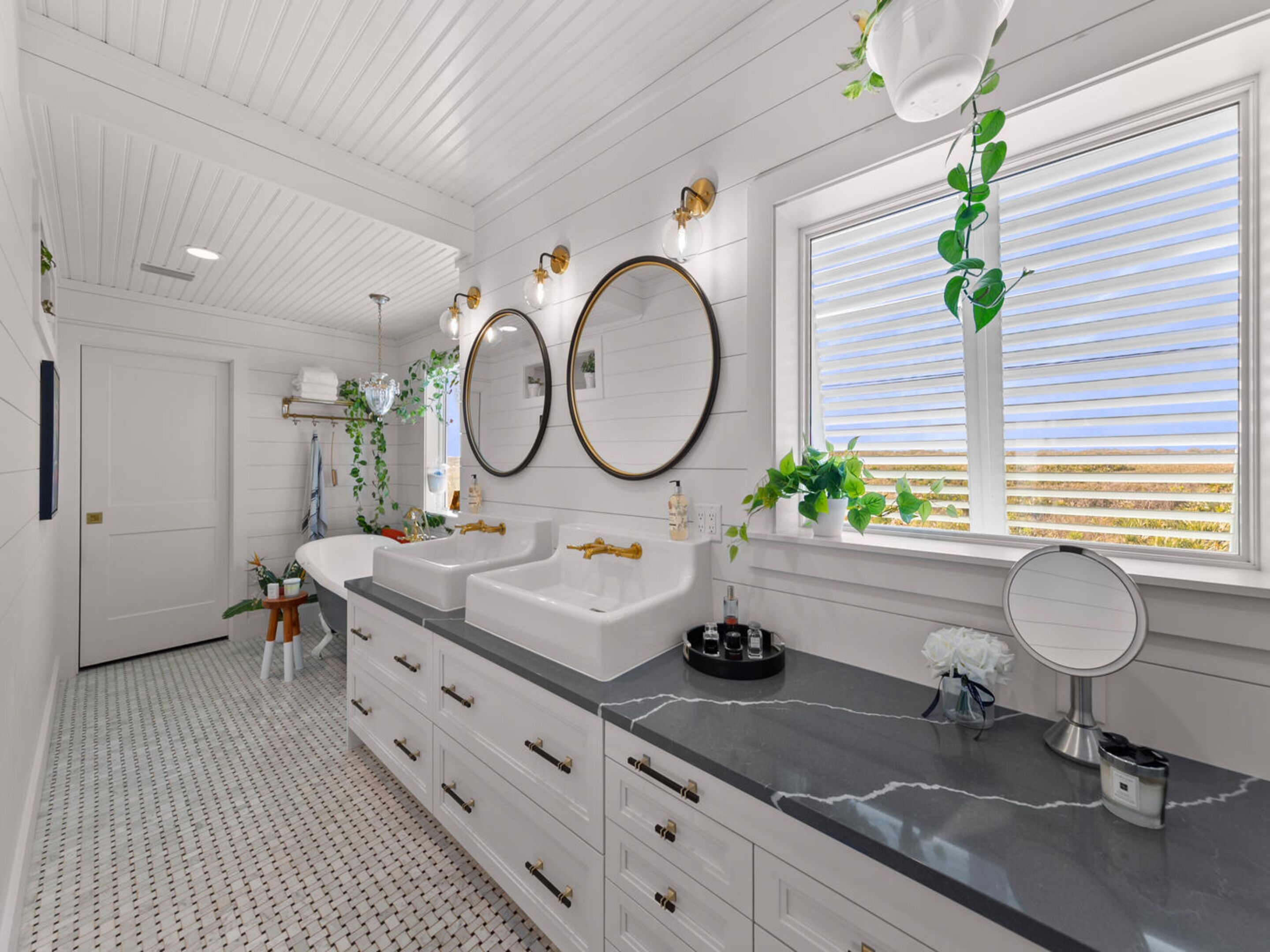 A modern bathroom with two sinks, a vanity, and a large window with blinds.