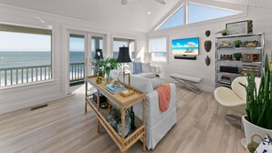 A spacious living room with a view of the ocean, a ceiling fan, and a bookshelf with decorative items. - Ocean Paradise by Distinctive Beach Rentals (Ponte Vedra Beach)