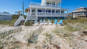A two-story beachfront house with a balcony, a staircase leading to the entrance, and several beach chairs. - Ocean Paradise by Distinctive Beach Rentals (Ponte Vedra Beach)