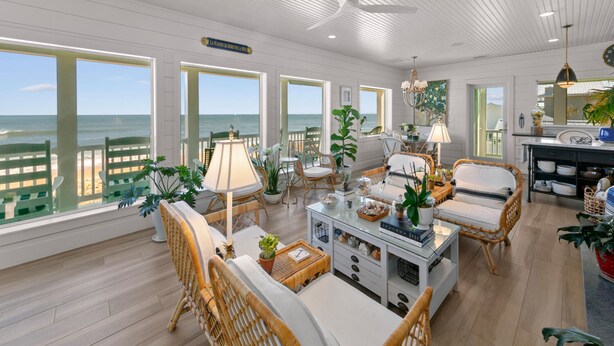 A spacious room with large windows overlooking the ocean, wicker furniture, and a ceiling fan. - Ocean Paradise by Distinctive Beach Rentals (Ponte Vedra Beach)