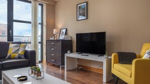 Una sala de estar moderna con un televisor grande, un sofá, un sillón amarillo y un escritorio con una lámpara.