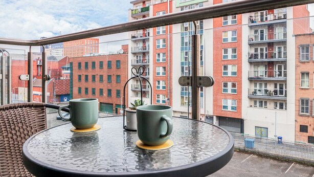 Un balcón con dos tazas verdes sobre una mesa de vidrio, con vistas a una hilera de edificios de apartamentos coloridos.