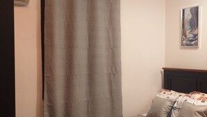 A bedroom with a bed, a curtain, a painting on the wall, and an air conditioning unit. - Your Cozy 1-bedroom, for short or long stays; minutes from the ocean and dining! (Dar es Salaam)