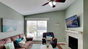 Ein Wohnzimmer mit braunem Ledersofa, einem Holztisch, einem Kamin, einem Fernseher und einem Deckenventilator.
