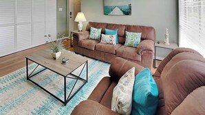 Ein Wohnzimmer mit braunem Sofa, einem Couchtisch, einer Lampe und einem Bild an der Wand.