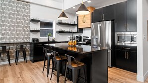 Una cocina moderna con una isla central, electrodomésticos de acero inoxidable, armarios negros e iluminación colgante.