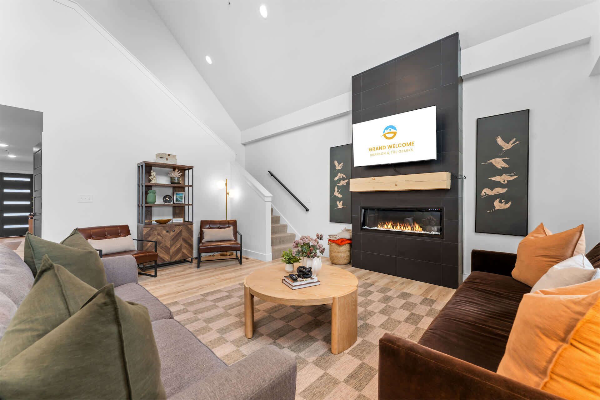 A modern living room with a fireplace, a television mounted on the wall, and a staircase leading to another level.